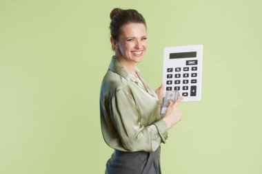 Gülümseyen orta yaşlı bir kadın elinde bir hesap makinesi tutuyor ve açık yeşil bir zemin üzerinde duran ve finansal zekâyı somutlaştıran Amerikan para birimine doğru hareket ediyor..