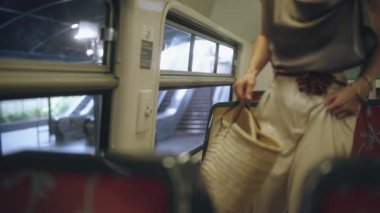 Gülümseyen bir kadın, Paris 'te seyahat ederken tren penceresinden manzaranın keyfini çıkarır. Elinde bir kamış çantası ve şık bir yaz elbisesi vardır..