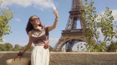 Havalı bir kadın Eyfel Kulesi 'nde selfie çekmek için gülümsüyor, güzel güneşli bir günde Paris' te tek başına seyahat anılarını yakalıyor..