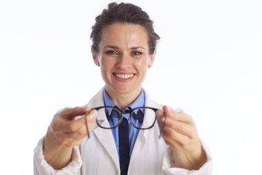 Beyaz laboratuvar önlüğü giyen neşeli bir kadın göz uzmanı, profesyonel görüş hizmetleri ve optometri hizmetlerini sembolize eden bir gözlük tutuyor..