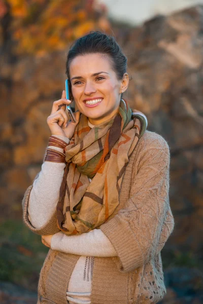 Woman talking mobile phone while walking in evening autumn park — Stock Photo, Image
