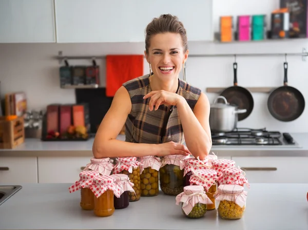 Happy, proud woman in kitchen with jars of home-preserved fruits — Stock Photo, Image