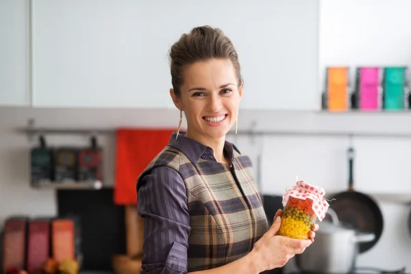 Smiling woman holding jar of vegetables in kitchen — Stock Image Smiling woman holding jar of vegetables in kitchen Stock Photo