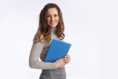 Bej balıkçı yaka ve ekose etekli gülümseyen bir kadın, mesleki hazırlık, eğitim ve modern iş yönetimini sembolize eden mavi bir klasör tutuyor..