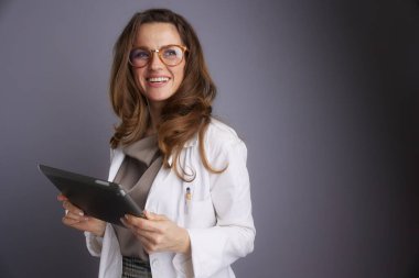 Beyaz laboratuvar önlüklü bir kadın doktor elinde sıcak bir gülümsemeyle dijital tablet tutuyor, tele-sağlık hizmetlerini ve modern klinik yönetimini temsil etmek için ideal..