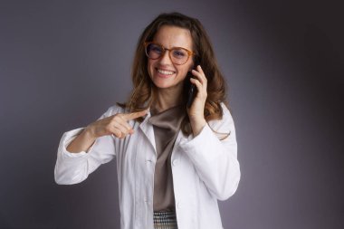 Beyaz önlüklü kendine güvenen bir doktor akıllı bir telefonla konuşuyor ve kamerayı işaret ediyor, kişisel sağlık hizmetleri tavsiyeleri ve profesyonel uzmanlığını iletiyor..