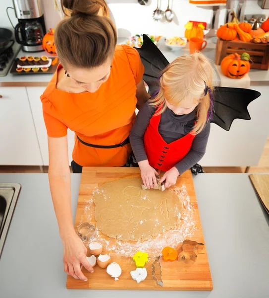 Girl in bat costume with mother making Halloween biscuits — Zdjęcie stockowe