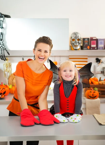 Mother with halloween dressed girl wearing oven mitts in kitchen — 스톡 사진