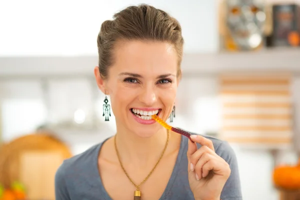 Smiling young woman eating halloween gummy worm candy — Stock Photo, Image