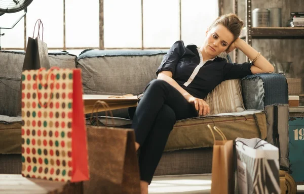 Unavený brunet žena sedící na gauči mezi nákupní tašky v podkroví — Stock fotografie