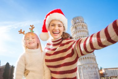 Mother in Christmas hat taking selfie with daughter in Pisa