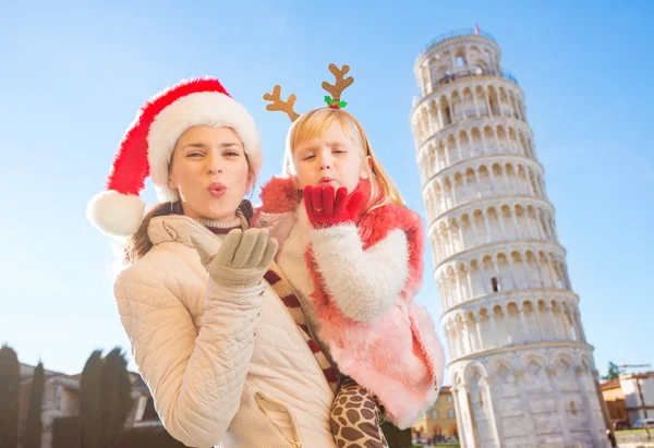 Mother in Christmas hat and daughter giving air kiss in Pisa