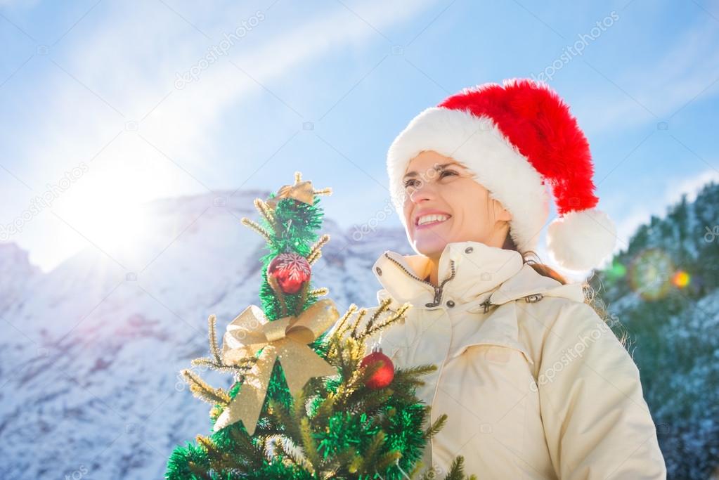 Happy young woman with Christmas tree in the front of mountains