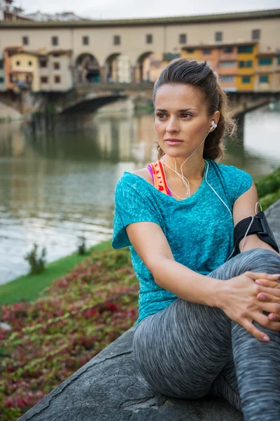 Sporty female with mp3 player sitting in front of Ponte Vecchio — Stock fotografie
