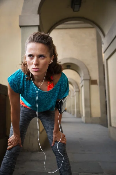 Sporty woman with earphones catching breath after jogging — Stock Photo, Image