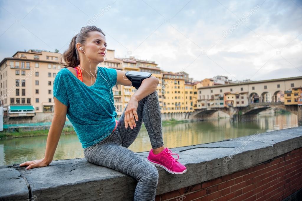 Fitness young woman sitting next to river with earphones