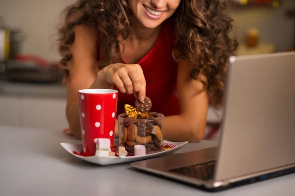 Mujer tomando una taza de chocolate caliente con galletas y usando un portátil —  Fotos de Stock