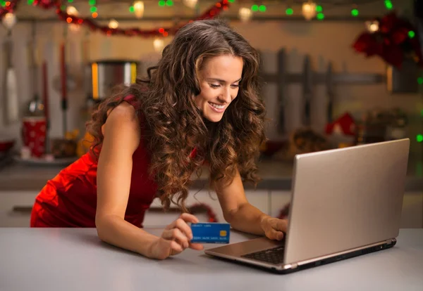 Woman with credit card typing on laptop in Christmas kitchen — Stock Photo, Image