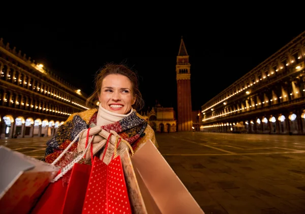 Happy woman holding shopping bags on Piazza San Marco in evening — Stock Photo, Image