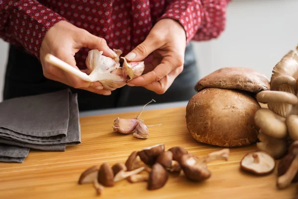 Vrouw handen scheiden teentjes knoflook met champignons — Stockfoto
