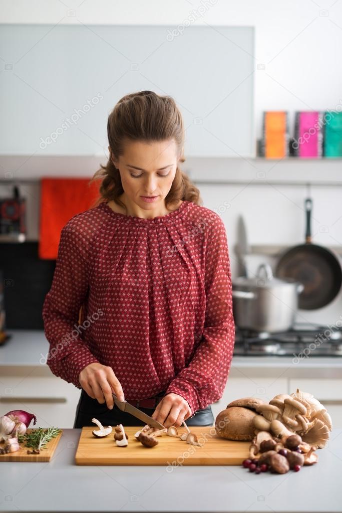 Woman in kitchen looking down while cutting mushrooms
