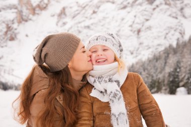 Mother kissing child outdoors among snow-capped mountains