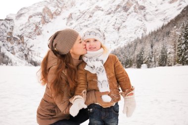 Mother kissing child outdoors among snow-capped mountains