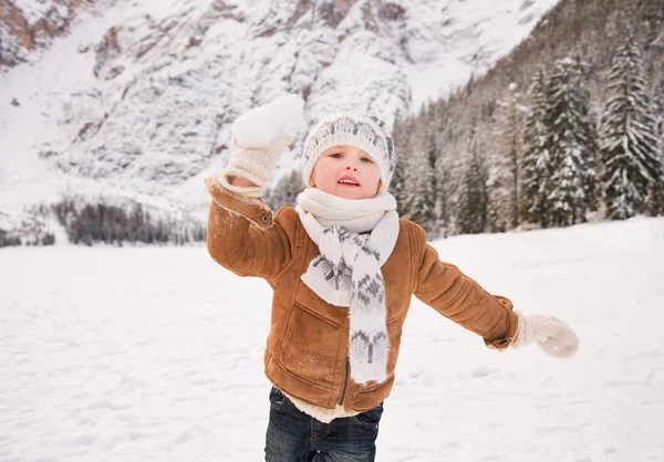 Niño lanzando bola de nieve al aire libre entre montañas cubiertas de nieve — Foto de Stock