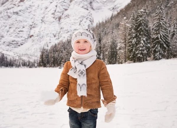 Child with snowball standing among snow-capped mountains — Stock Photo, Image