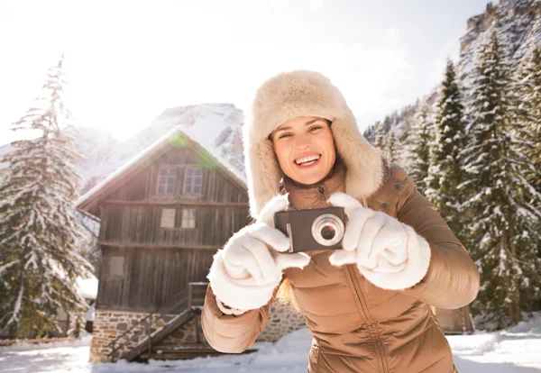 Smiling woman standing near mountain house and taking photos — 图库照片