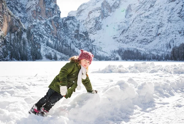Criança brincando com a neve na frente de montanhas nevadas — Fotografia de Stock