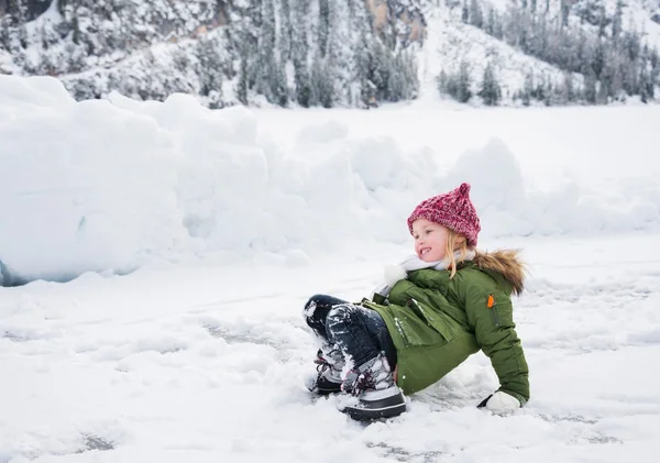 Criança feliz em casaco verde caiu enquanto brincava na neve . — Fotografia de Stock