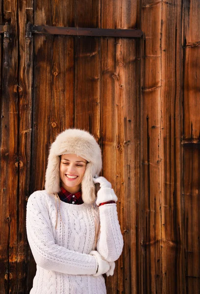 Woman in white knitted sweater standing near rustic wood wall — Stockfoto