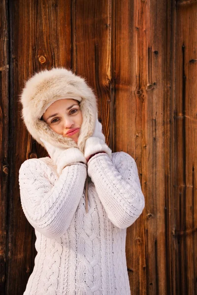 Happy woman fooling around with furry hat near rustic wood wall — Zdjęcie stockowe