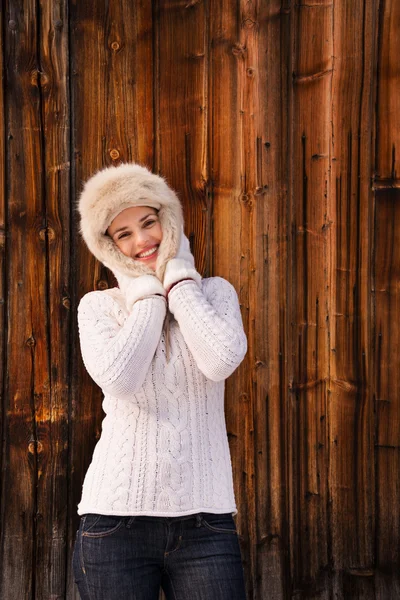 Glückliche Frau im Strickpullover, die neben rustikaler Holzwand steht — Stockfoto