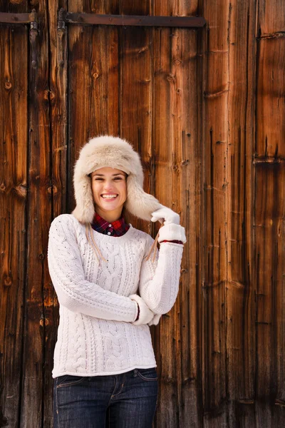 Woman in white knitted sweater and furry hat near wood wall — Stock fotografie