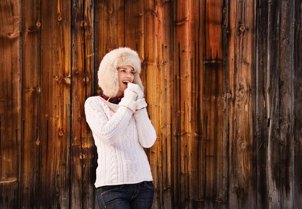 Smiling woman blowing warm breath on her hands near wood wall — Φωτογραφία Αρχείου