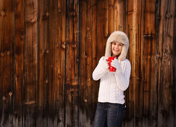 Happy woman in knitted sweater with cup near rustic wood wall — Zdjęcie stockowe