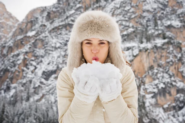 Женщина в меховой шапке выдувает снег из рук в камеру на открытом воздухе — стоковое фото