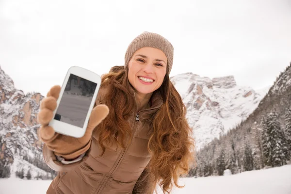 Woman outdoors among snow-capped mountains showing cell phone — ストック写真