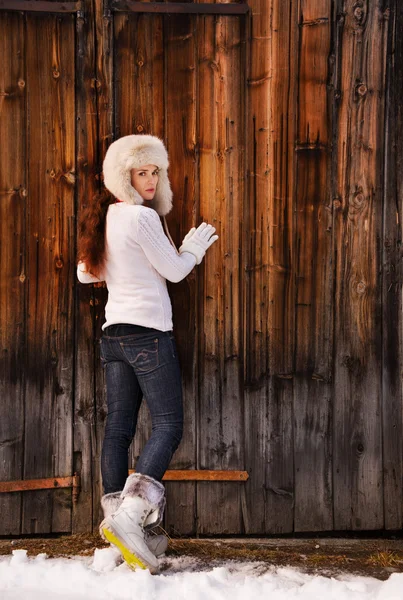 Mulher de camisola branca e chapéu peludo posando perto da parede de madeira — Fotografia de Stock