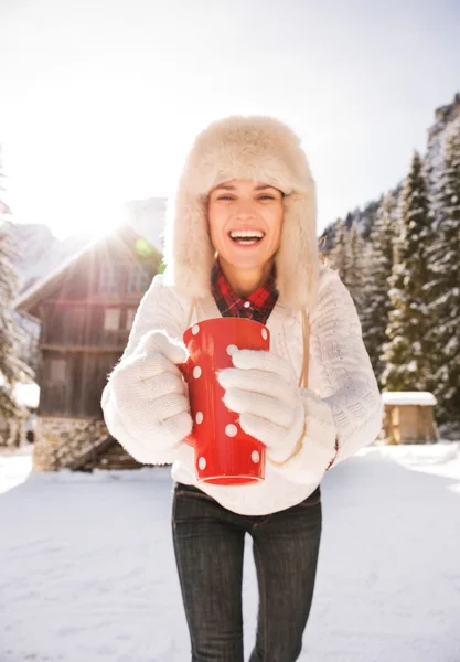 Primer plano en la taza roja en las manos de la mujer sonriente cerca de la casa de montaña — Foto de Stock