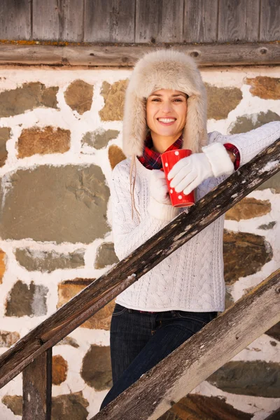 Glückliche Frau mit Pokal steht auf Treppe des gemütlichen Berghauses — Stockfoto