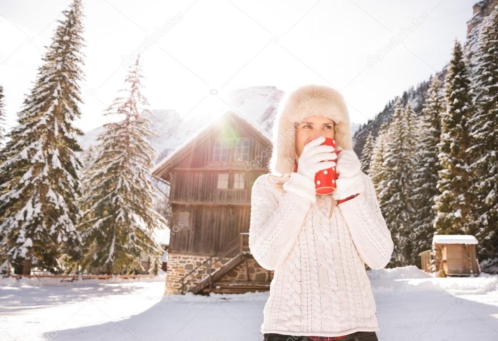 Woman in white sweater enjoying hot beverage near mountain house