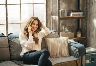 Divan'da oturan ve akıllı telefon konuşan gülümseyen şık kadın