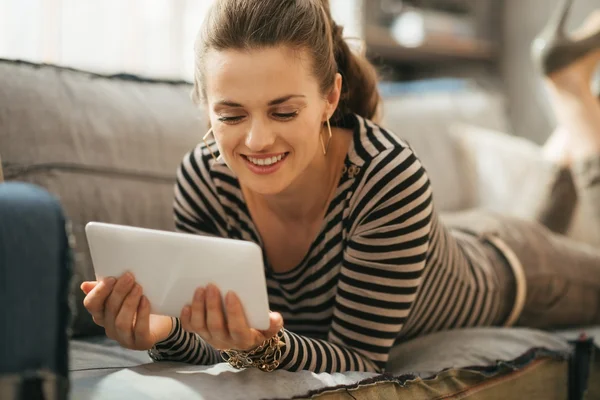Счастливая молодая женщина лежит на диване и держит планшетный компьютер — стоковое фото
