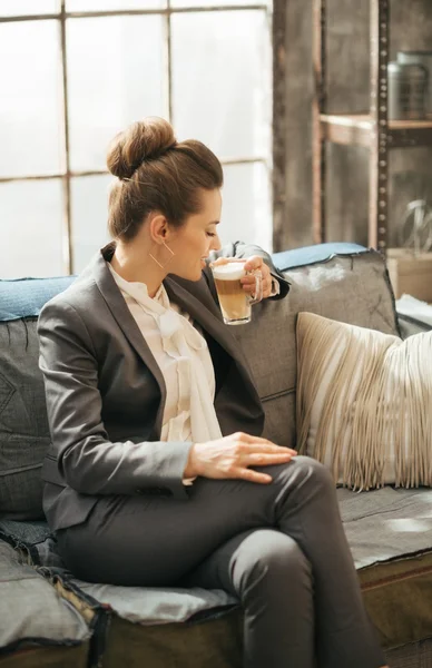 Geschäftsfrau sitzt auf Sofa und trinkt Kaffee auf Dachboden — Stockfoto