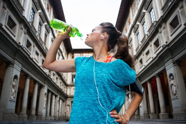 Sporty woman with headset is drinking water from the bottle — Zdjęcie stockowe