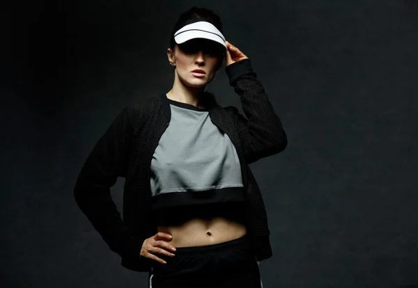 Young fit woman adjusting tennis visor against dark background — Stock Photo, Image