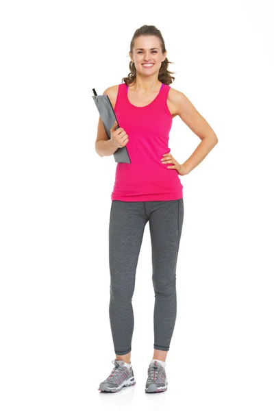 Full length portrait of smiling fitness young woman writing in clipboard and looking on copy space — Stock Photo, Image